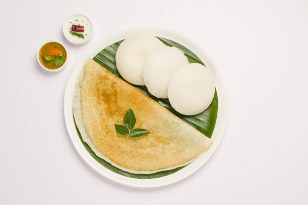 白を基調にバナナの葉とカレーをサンドしたホワイトプレートに美しく盛り付けられた南インドのメイン朝食アイテム「グヒローストドサ」と「イドリイ」. - 写真・画像
