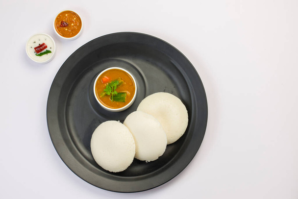 Idly o Idli, el desayuno principal indio del sur que se arregla maravillosamente en un plato negro sobre fondo blanco. - Foto, Imagen