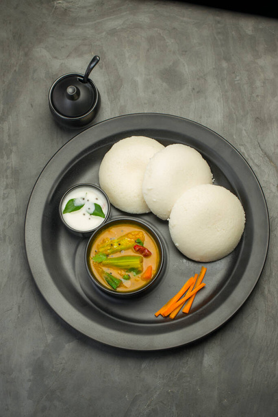 Idly o Idli, el desayuno principal indio del sur que está bellamente organizado en un plato negro con textura de color gris con fondo de cocina. - Foto, Imagen