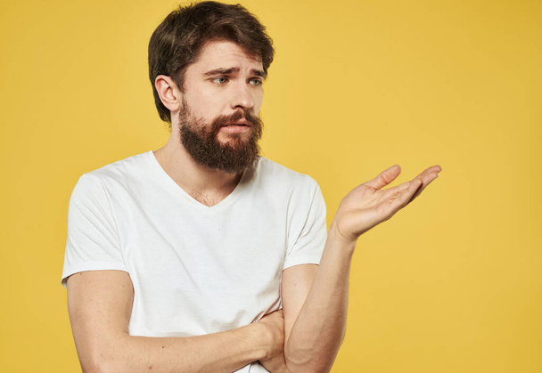 A man in a white t-shirt gestures with his hands on a yellow background cropped view - Foto, immagini