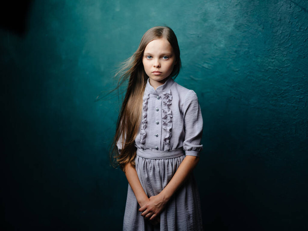 Encantadora chica con el pelo suelto sobre un fondo turquesa en un vestido gris - Foto, Imagen