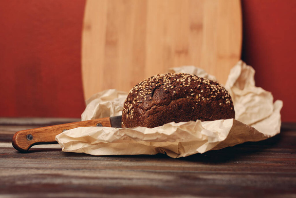 pão escuro de centeio com uma faca em um pacote de papel imagem de textura de mesa de madeira - Foto, Imagem