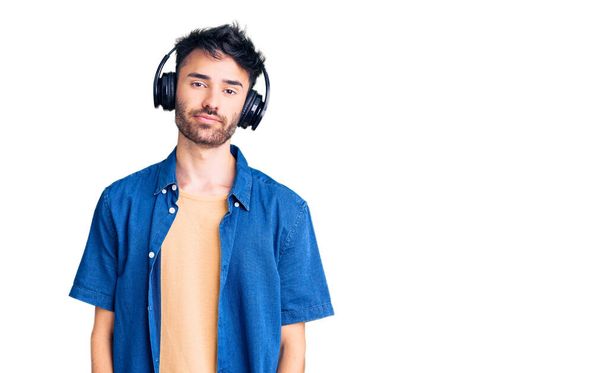 Joven hispano escuchando música usando auriculares con expresión seria en la cara. simple y natural mirando a la cámara.  - Foto, imagen