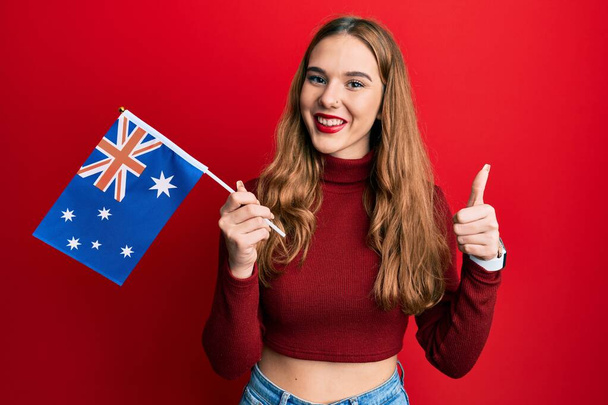Молода блондинка тримає австралійський прапор усміхнений щасливий і позитивний, великий палець робить відмінний знак схвалення
  - Фото, зображення