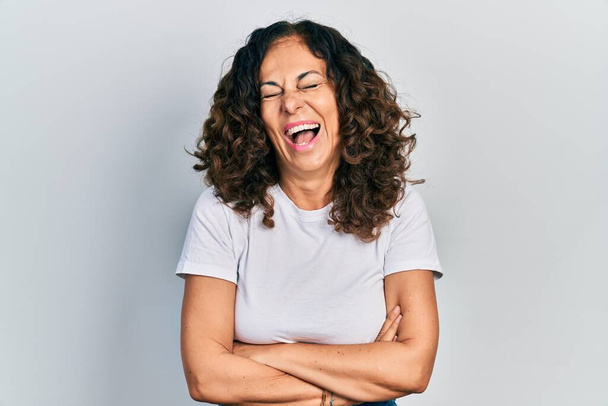Mujer hispana de mediana edad con los brazos cruzados gesto sonriendo y riendo en voz alta porque broma loca divertida.  - Foto, imagen