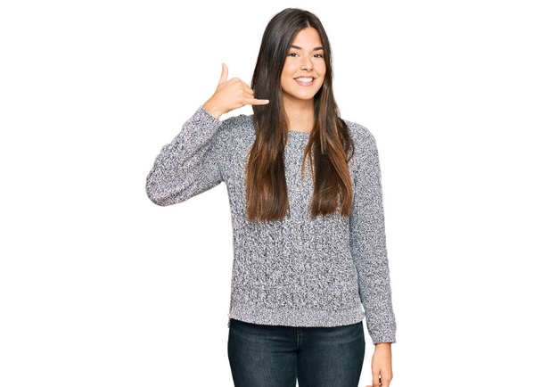 Mujer morena joven vistiendo suéter casual de invierno sonriendo haciendo gesto de teléfono con la mano y los dedos como hablando por teléfono. comunicar conceptos.  - Foto, Imagen