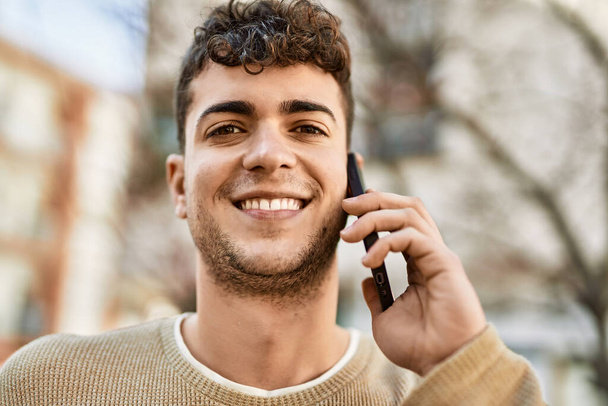 Молодий іспаномовний чоловік посміхається щасливим розмовляти по смартфону в місті
 - Фото, зображення