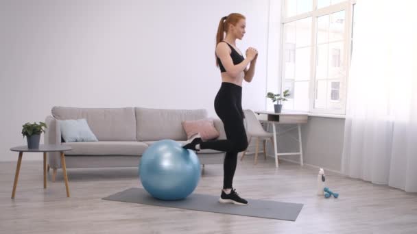 Deportiva mujer haciendo sentadillas de una pierna con Fitball haciendo ejercicio en casa - Metraje, vídeo