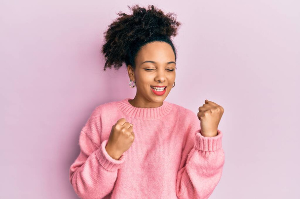 Молодая африканская американка, одетая в повседневную одежду, радуется удивлению и удивлению за успех с поднятыми руками и закрытыми глазами  - Фото, изображение