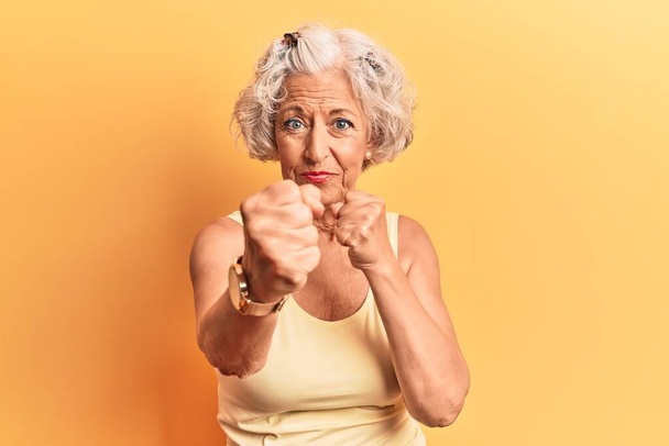 Mujer mayor de cabello gris con ropa casual golpeando puño para luchar, ataque agresivo y enojado, amenaza y violencia  - Foto, Imagen