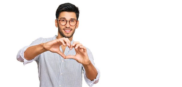 Young handsome man wearing casual clothes and glasses smiling in love doing heart symbol shape with hands. romantic concept.  - Fotografie, Obrázek