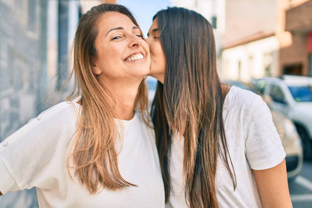 Beautiful hispanic mother and daughter kissing at the city. - 写真・画像