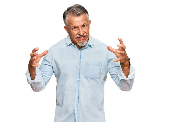 Grauhaariger Mann mittleren Alters in lässiger Kleidung, der frustriert vor Wut schreit, Hände, die versuchen zu würgen, verrückt schreit  - Foto, Bild