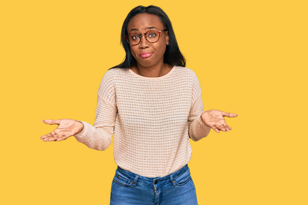 Junge schwarze Frau in lässiger Kleidung und Brille, ahnungslos und verwirrt mit erhobenen Armen und Händen. Zweifelhaftes Konzept.  - Foto, Bild