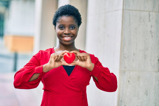 Fiatal afro-amerikai nő mosolyog boldog gazdaság szív áll a városban. - Fotó, kép