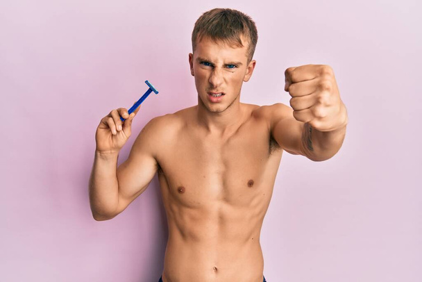 Young caucasian man shirtless holding razor annoyed and frustrated shouting with anger, yelling crazy with anger and hand raised  - Foto, immagini
