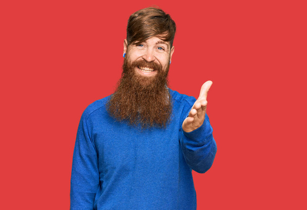Νεαρός Ιρλανδός κοκκινομάλλης άνδρας φορώντας casual ρούχα χαμογελώντας φιλικό προσφέροντας χειραψία ως χαιρετισμό και φιλόξενο. επιτυχημένη επιχείρηση.  - Φωτογραφία, εικόνα