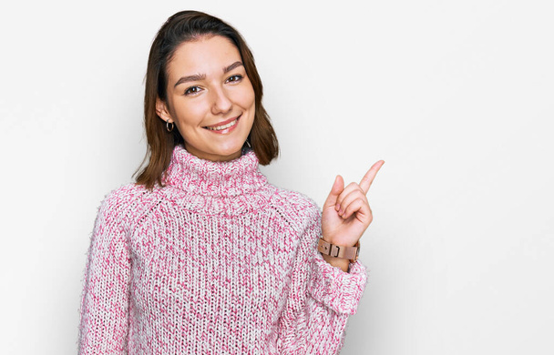 Young caucasian girl wearing wool winter sweater with a big smile on face, pointing with hand finger to the side looking at the camera.  - Foto, Imagem