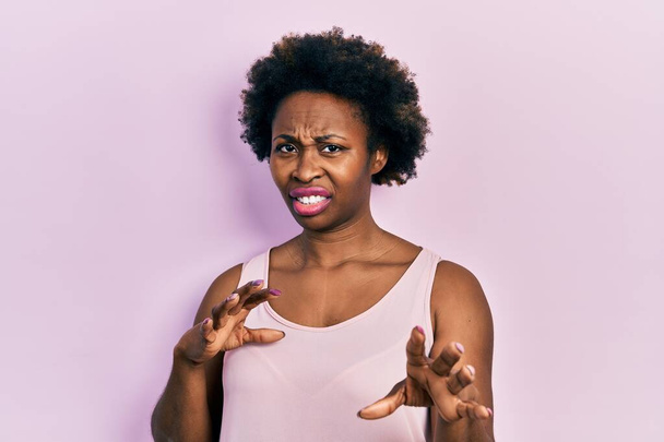 Молода афро-американська жінка, одягнена в звичайну безрукаву сорочку огидного виразу, незадоволена і страшна, що чинить огиду обличчя, тому що реагує відразливо. підняті руки.  - Фото, зображення