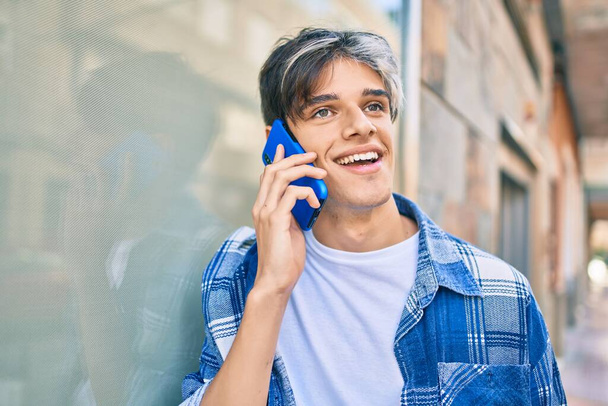 Jonge Spaanse man glimlachend gelukkig praten op de smartphone in de stad. - Foto, afbeelding