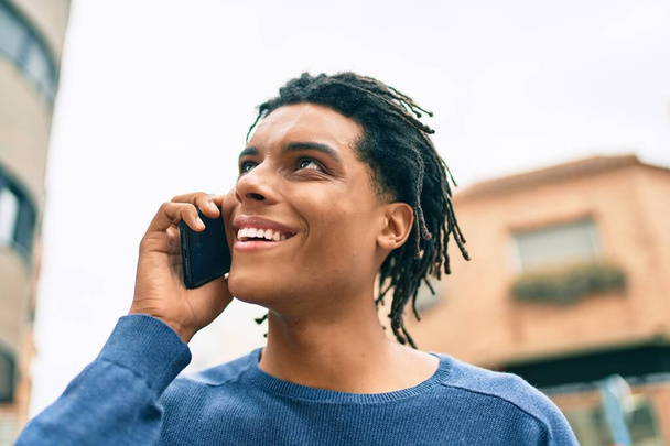 Giovane uomo afroamericano sorridente felice parlando sullo smartphone in strada della città. - Foto, immagini