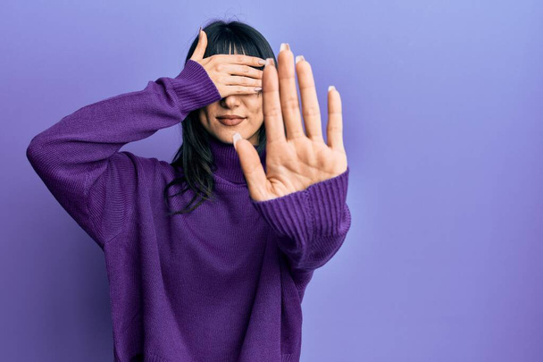 Young brunette woman with bangs wearing turtleneck sweater covering eyes with hands and doing stop gesture with sad and fear expression. embarrassed and negative concept.  - Photo, Image
