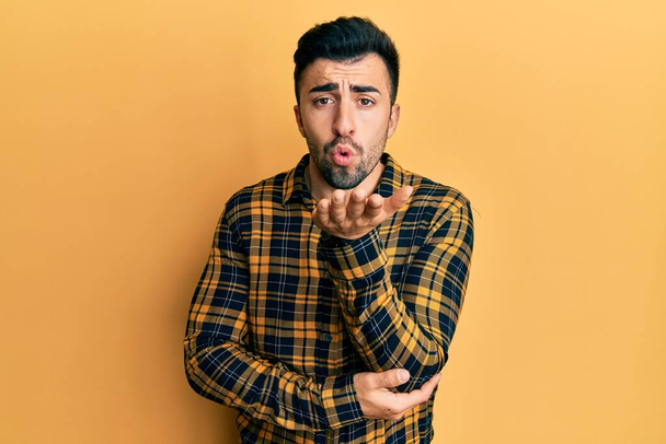 Young hispanic man wearing casual clothes looking at the camera blowing a kiss with hand on air being lovely and sexy. love expression.  - 写真・画像