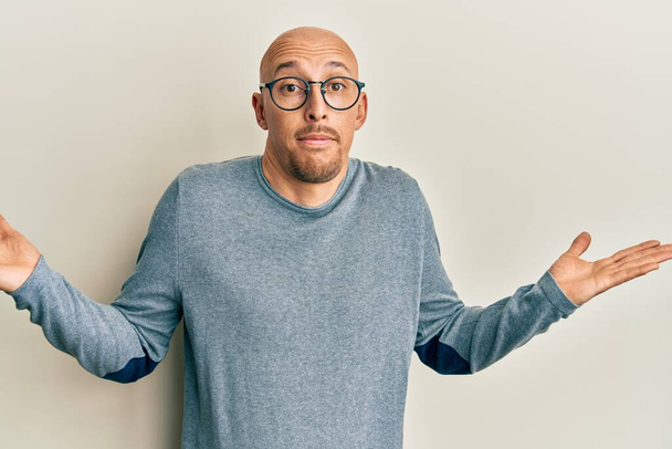 Bald man with beard wearing casual clothes and glasses clueless and confused with open arms, no idea and doubtful face.  - Photo, Image