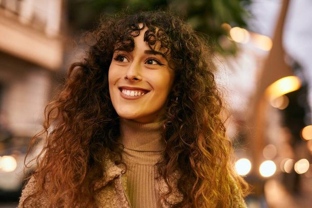 Μια νεαρή Ισπανίδα χαμογελαστή ευτυχισμένη στέκεται στην πόλη. - Φωτογραφία, εικόνα