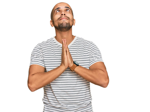 Hombre adulto hispano vestido con ropa casual mendigando y rezando con las manos juntas con expresión de esperanza en la cara muy emocional y preocupado. mendicidad.  - Foto, Imagen
