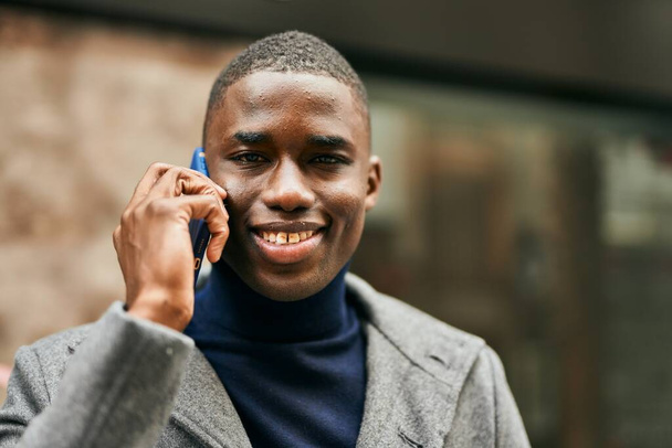 Giovane uomo afroamericano sorridente felice parlando sullo smartphone in città - Foto, immagini