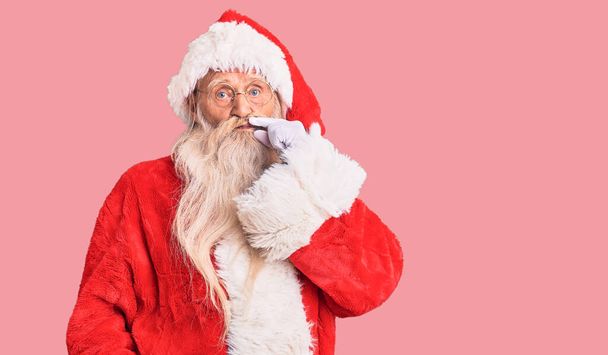 Старик с седыми волосами и длинной бородой в традиционном костюме Санта Клауса рот и губы закрыты как молния с пальцами. секретный и молчаливый, табу говорить  - Фото, изображение