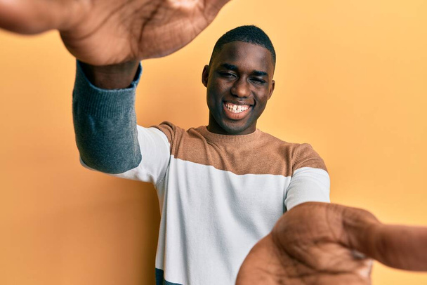 Fiatal afro-amerikai férfi alkalmi ruhában, nyitott karokkal mosolyogva nézi a kamerát. vidám kifejezés, mely felöleli a boldogságot.  - Fotó, kép