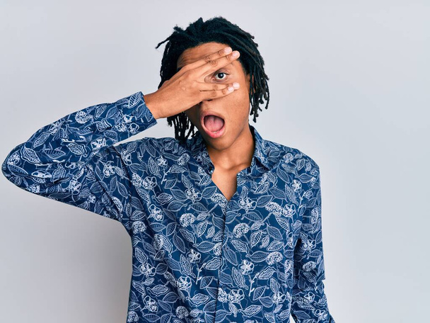 Mladý afroameričan v tričku ve stylu 80. let vykukuje v šoku, zakrývá obličej a oči rukou, dívá se prsty s rozpačitým výrazem.  - Fotografie, Obrázek