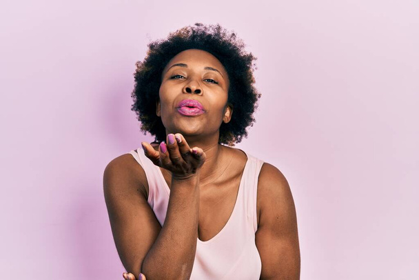 Young african american woman wearing casual sleeveless t shirt looking at the camera blowing a kiss with hand on air being lovely and sexy. love expression.  - Photo, Image