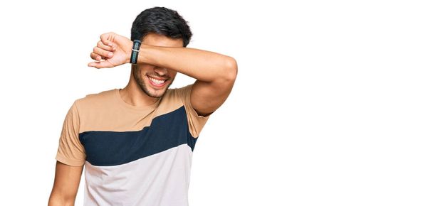 Young handsome man wearing casual clothes covering eyes with arm smiling cheerful and funny. blind concept.  - Фото, изображение