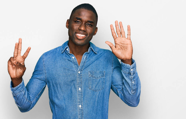 Fiatal afro-amerikai férfi alkalmi ruhát visel, mutatva és mutatva ujjaival 8-as szám, miközben mosolyogva magabiztos és boldog.  - Fotó, kép