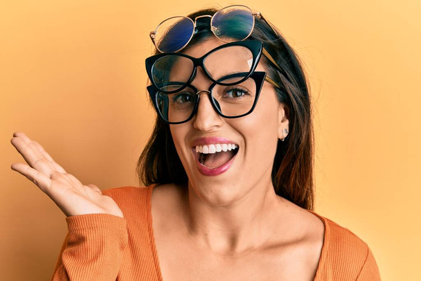 Beautiful hispanic woman wearing many glass over face celebrating achievement with happy smile and winner expression with raised hand  - Foto, immagini
