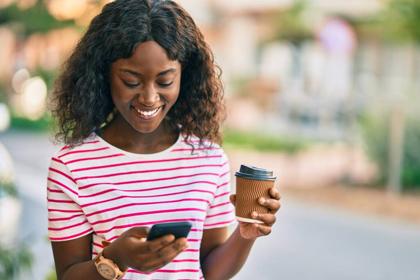 Молодая африканская американка, пьющая смартфон, уносит кофе в город. - Фото, изображение