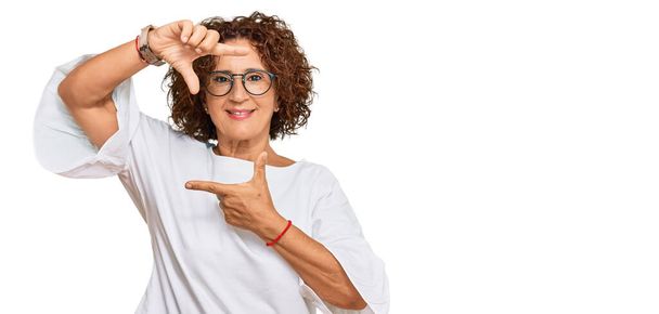 Beautiful middle age mature woman wearing casual clothes and glasses smiling making frame with hands and fingers with happy face. creativity and photography concept.  - Photo, Image