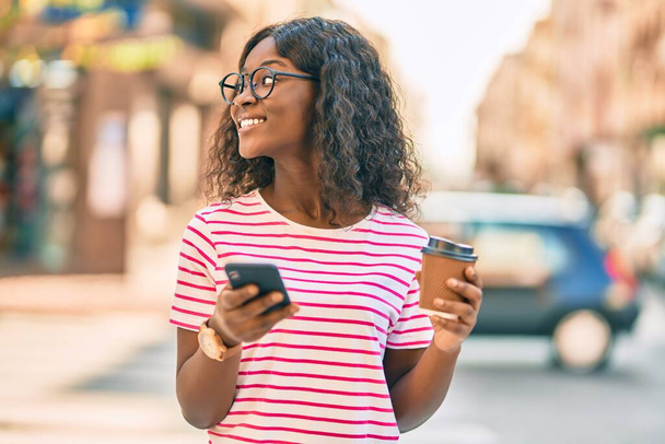 Joven afroamericana chica usando smartphone bebiendo café en la ciudad. - Foto, Imagen