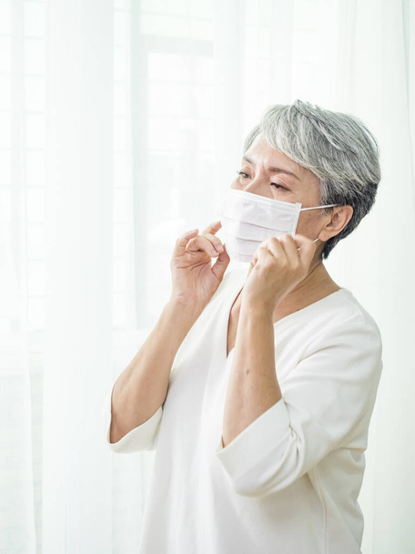 Старшая азиатка в маске во время коронавируса и вспышки гриппа. Защита от вирусов и болезней, домашний карантин. COVID-2019. Снимать или снимать маски. - Фото, изображение