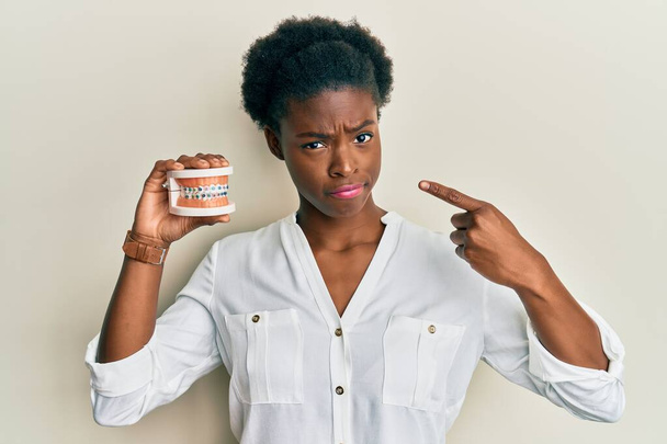 Mladá africká americká dívka držící ortodontickou skeptičku a nervózně se mračí kvůli problému. negativní osoba.  - Fotografie, Obrázek