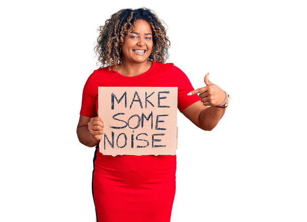 Young african american plus size woman holding make some noise banner smiling happy pointing with hand and finger  - Photo, Image