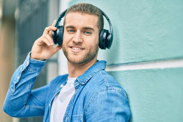Jovem caucasiano sorrindo feliz usando fones de ouvido na cidade. - Foto, Imagem