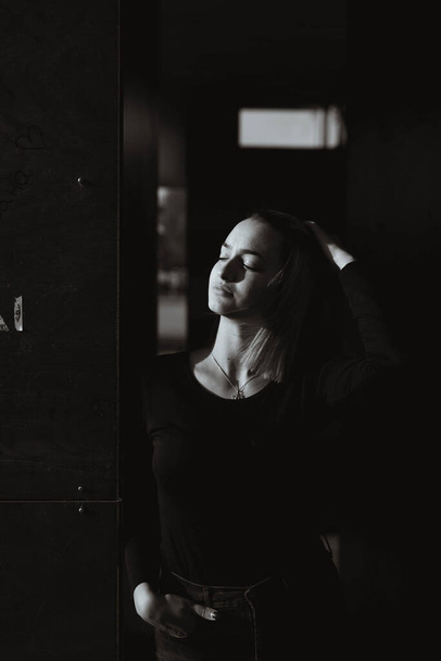 A vertical grayscale shot of a caucasian female posing in a dark room - Zdjęcie, obraz