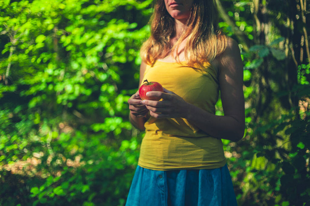 Genç bir kadın bir elmayla ormanda duruyor. - Fotoğraf, Görsel