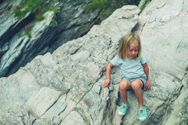 A little preschooler is climbing rocks on the beach - Фото, изображение