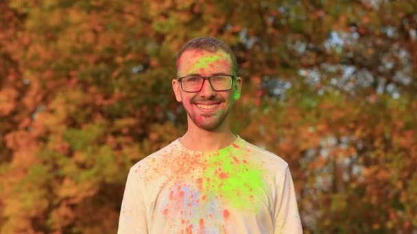 Radosny brodaty mężczyzna w okularach w doskonałym nastroju w holi kolorów na festiwalu  - Materiał filmowy, wideo