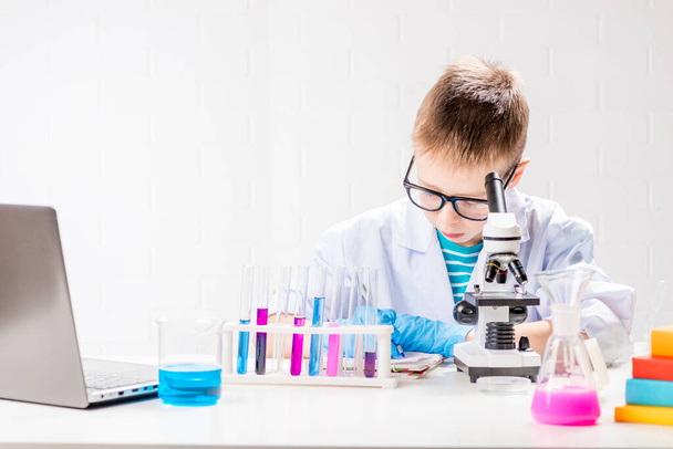 A schoolboy with a microscope examines chemicals in test tubes, conducts experiments - a portrait on a white background. Concept for the study of coronavirus in the laboratory - Photo, Image